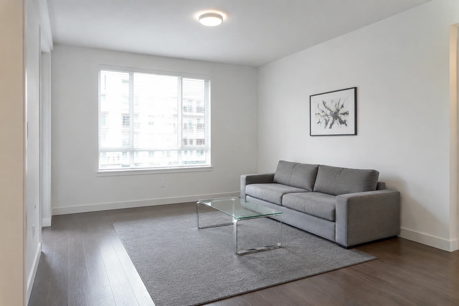 A stark minimalist living room from the 2010s with white walls, a gray sofa, a glass table and almost nothing else