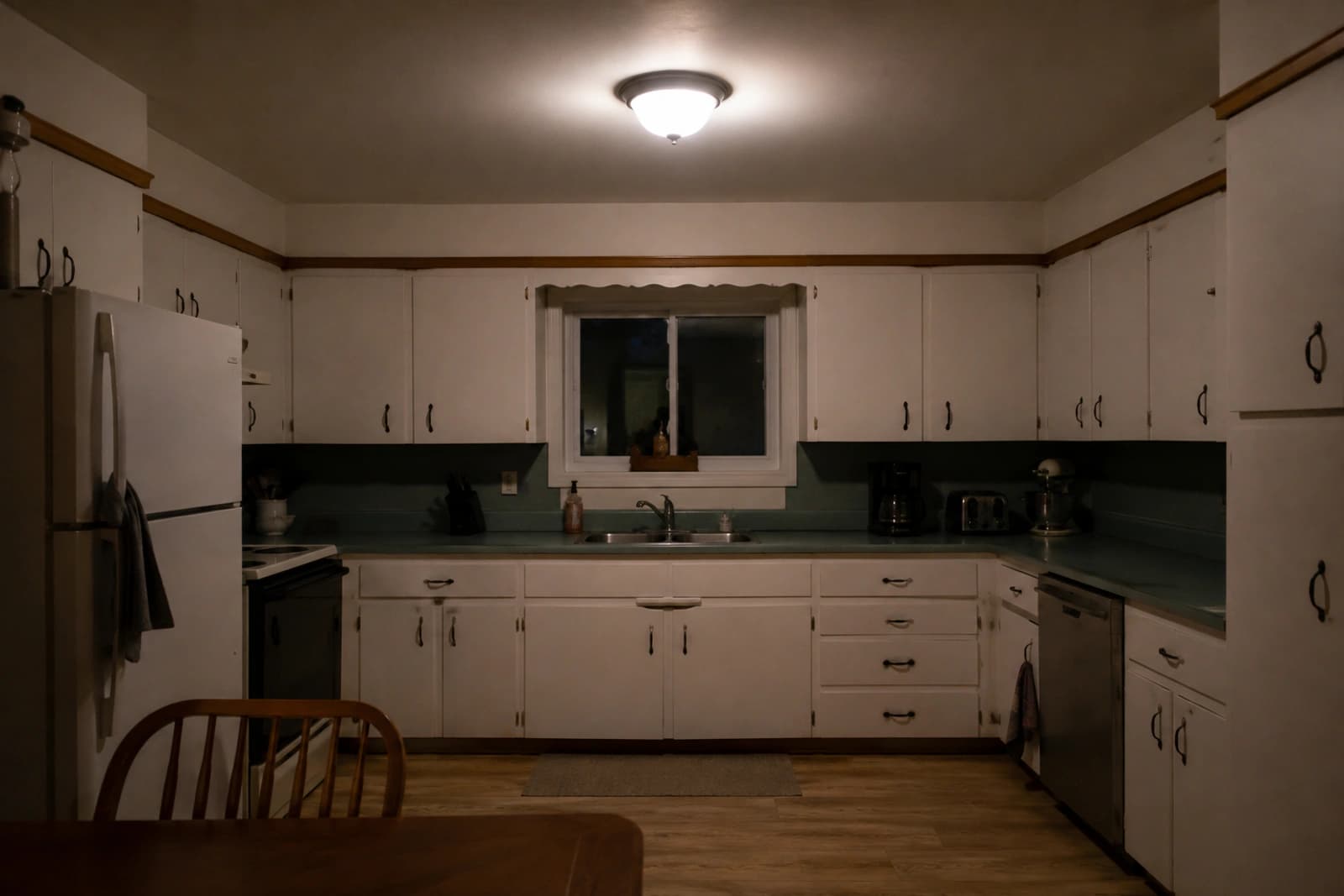 A kitchen lit by a single ceiling fixture, with dark shadows on the counters and under the cabinets