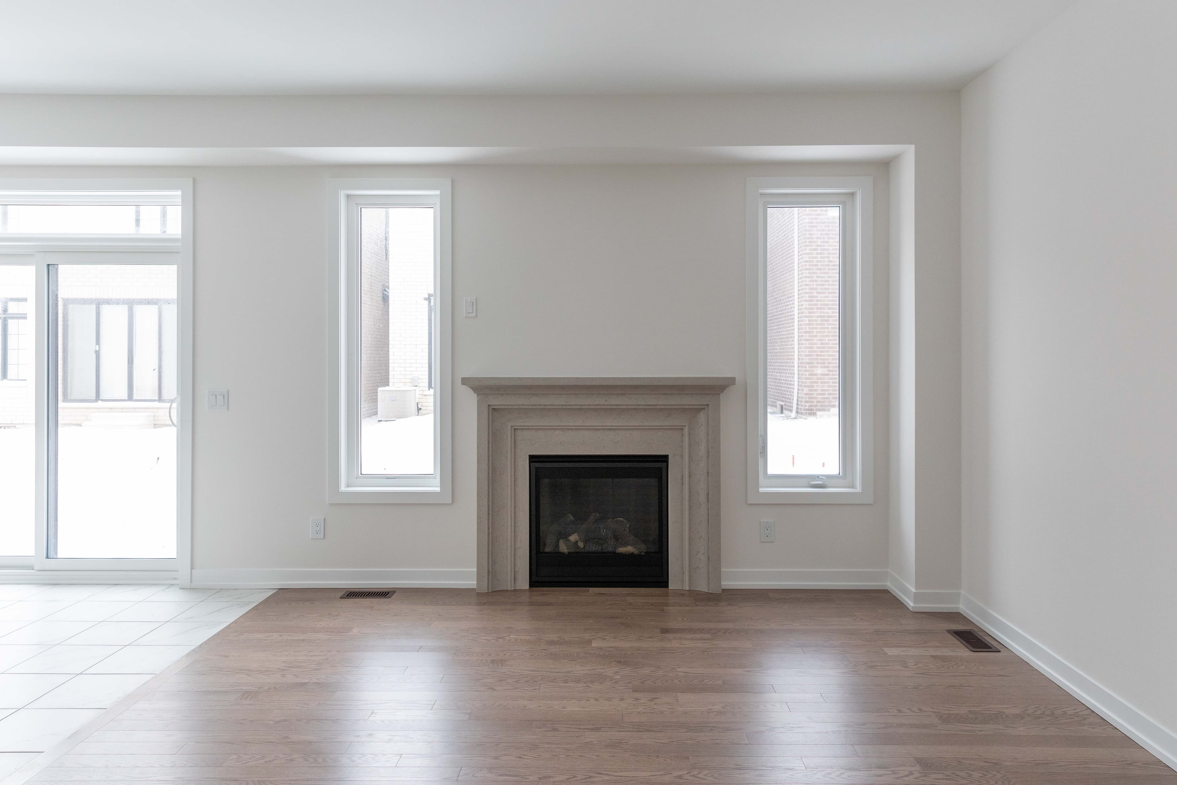 An empty living room with white walls, a stone fireplace and wood floors