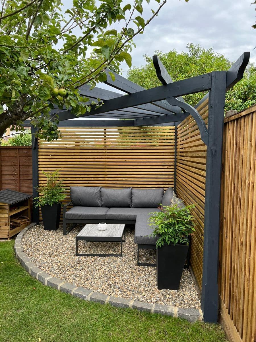 A backyard pergola with a gray corner sofa on a gravel patio